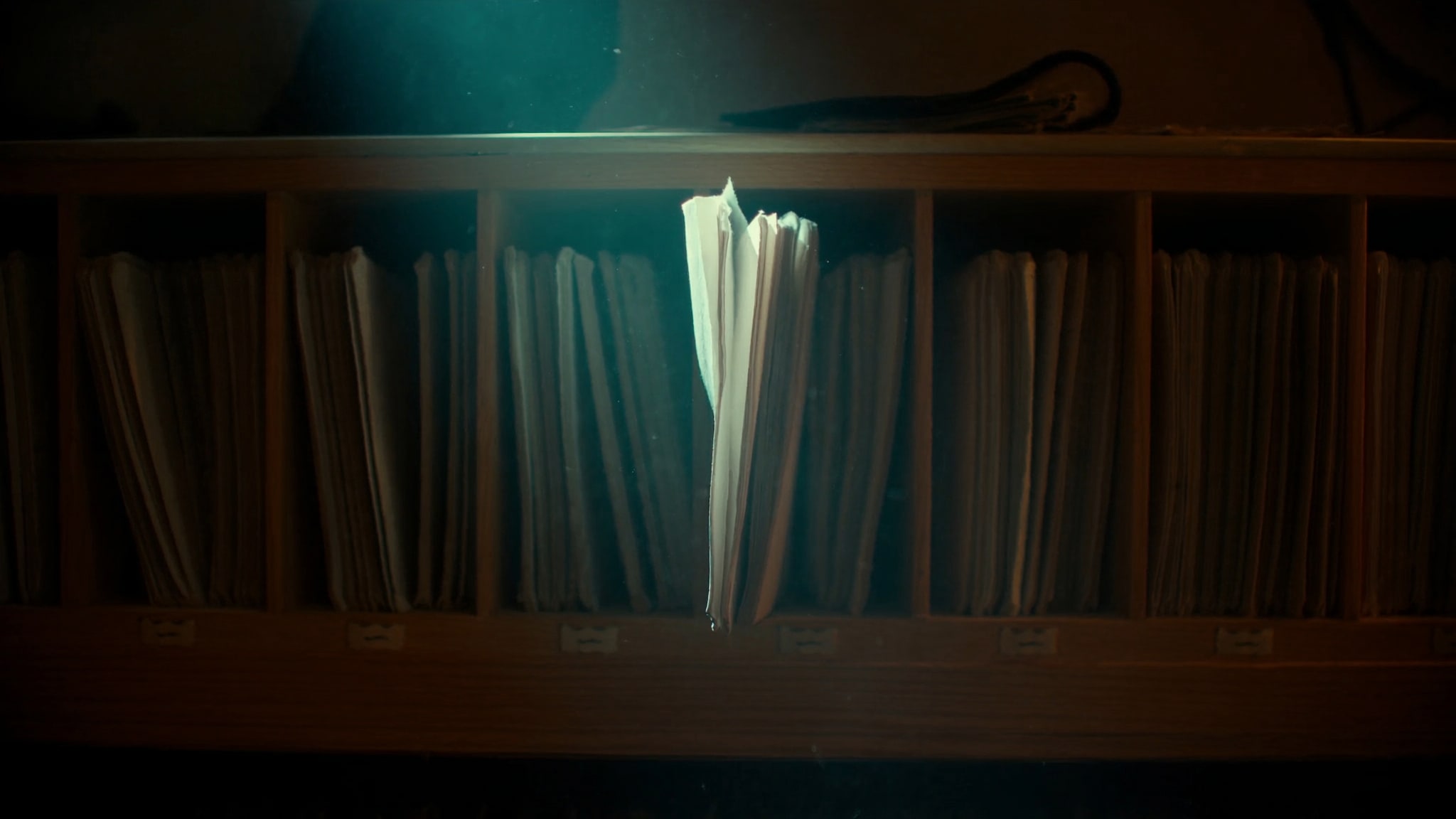 Step-Header: dunkles Archivregal voller geschlossener Mappen, eine einzelne halb herausgezogen im Lichtstrahl
