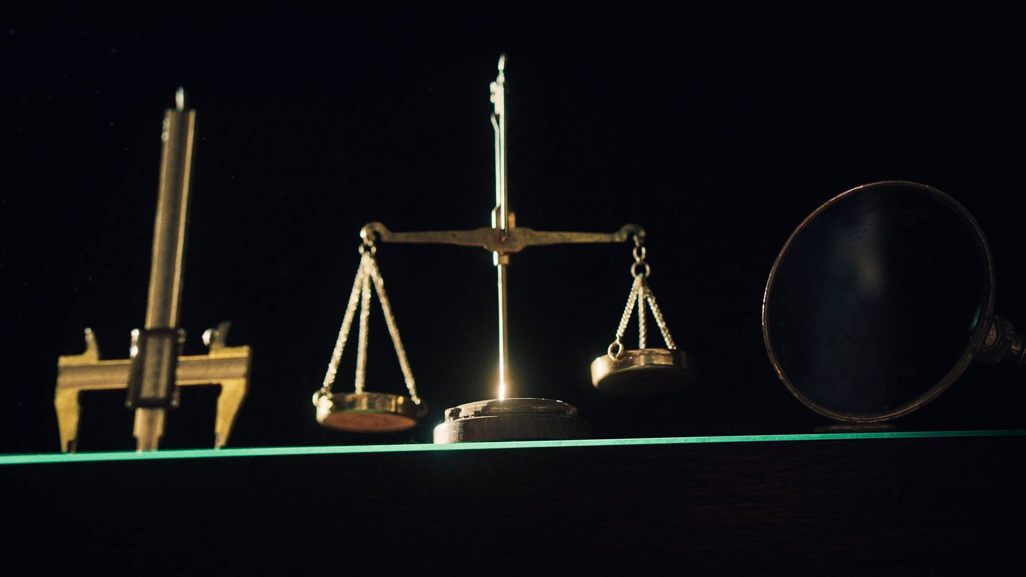 Drei Messwerkzeuge nebeneinander auf dunklem Holz: Messschieber, Waage, Lupe