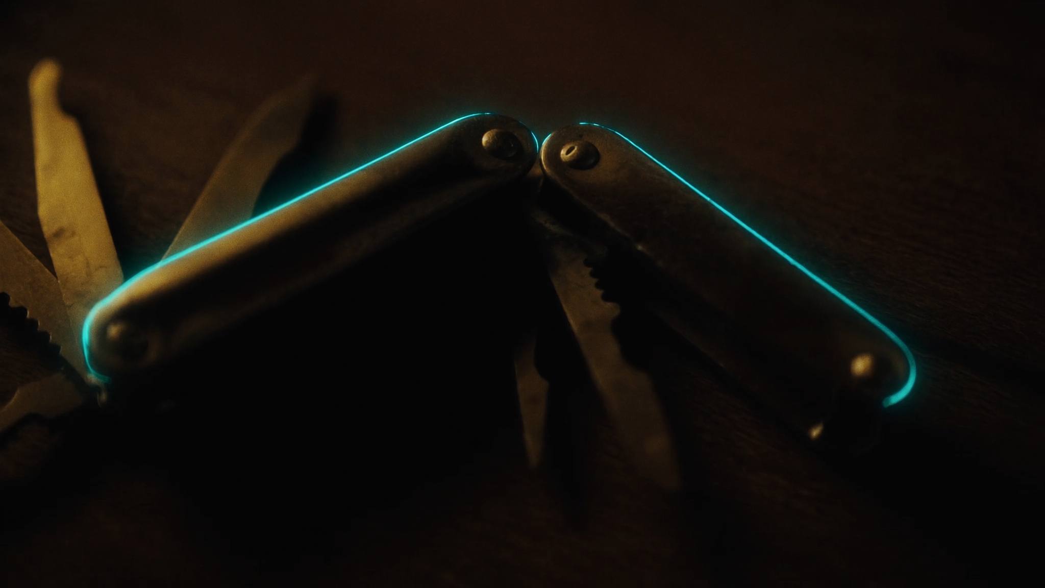 Aufgeklapptes Messing-Mehrzweckwerkzeug mit mehreren Klingen, teal leuchtende Kanten