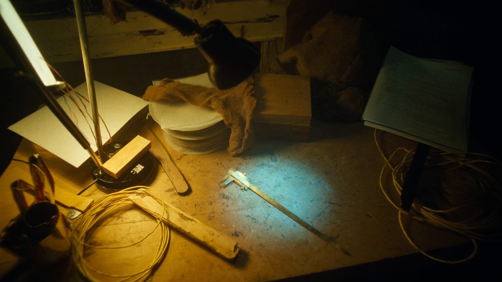 Eine überfüllte dunkle Werkbank, in einem schmalen Lichtkegel liegt ein einzelnes Werkzeug frei