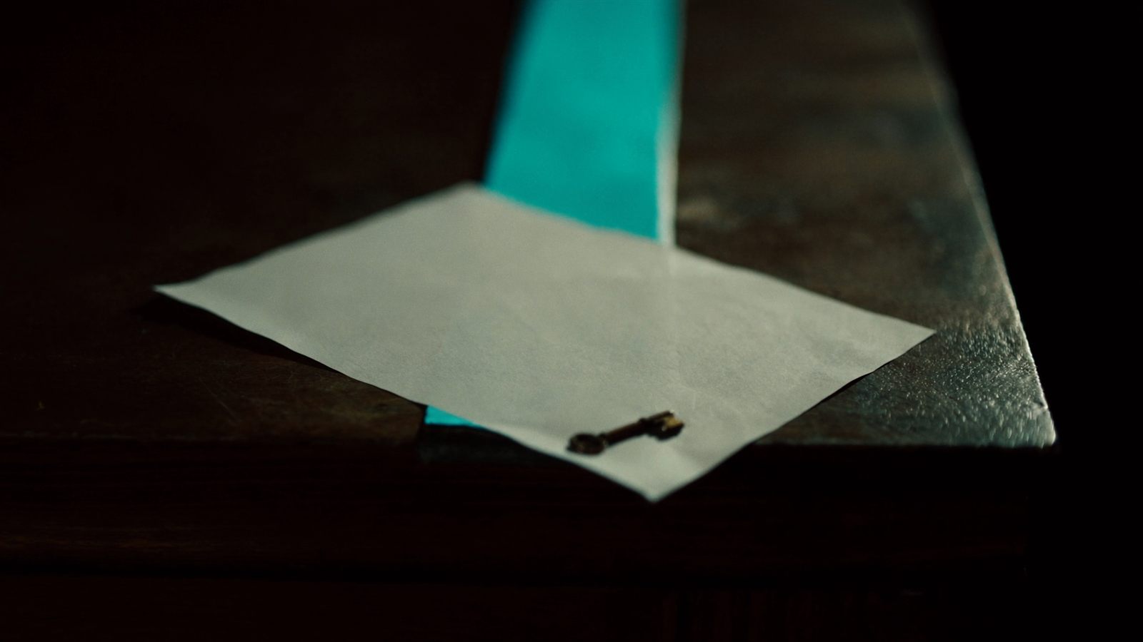 Ein gefaltetes Blatt und ein Messingschlüssel liegen auf dunklem Holz an der Kante eines Lichtkegels