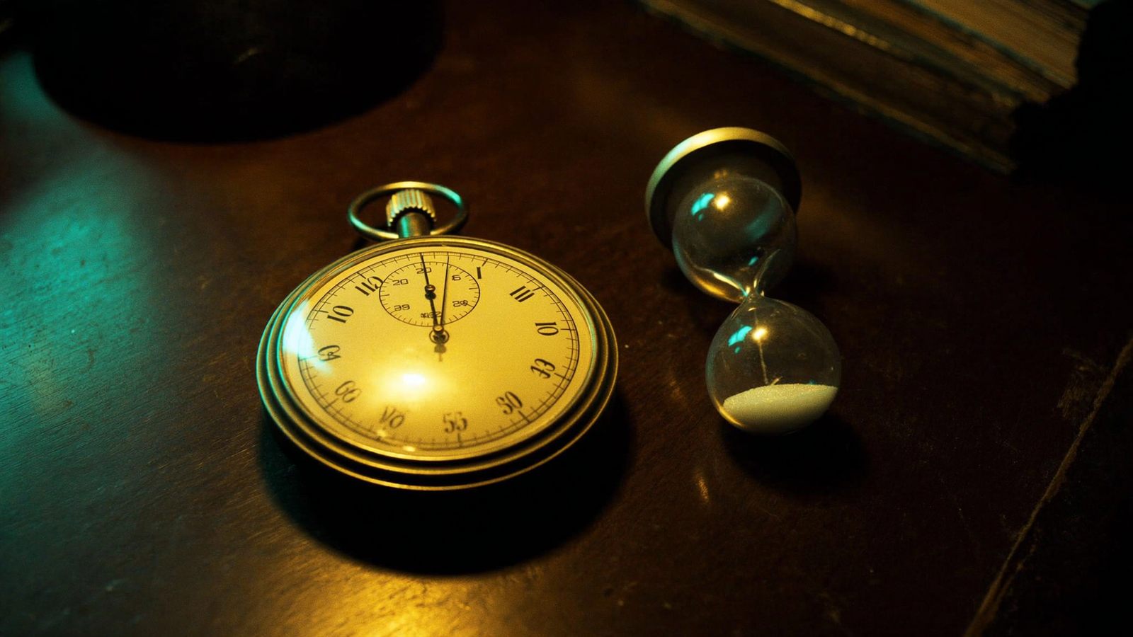 Eine Stoppuhr aus Messing liegt neben einer umgedrehten Sanduhr